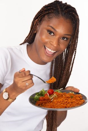 black girl wearing white t shirt smiling, jollof in plate and eating jollof with fork